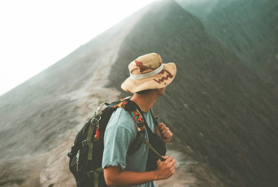 man in brown hat and blue denim jacket standing on mountain during daytime